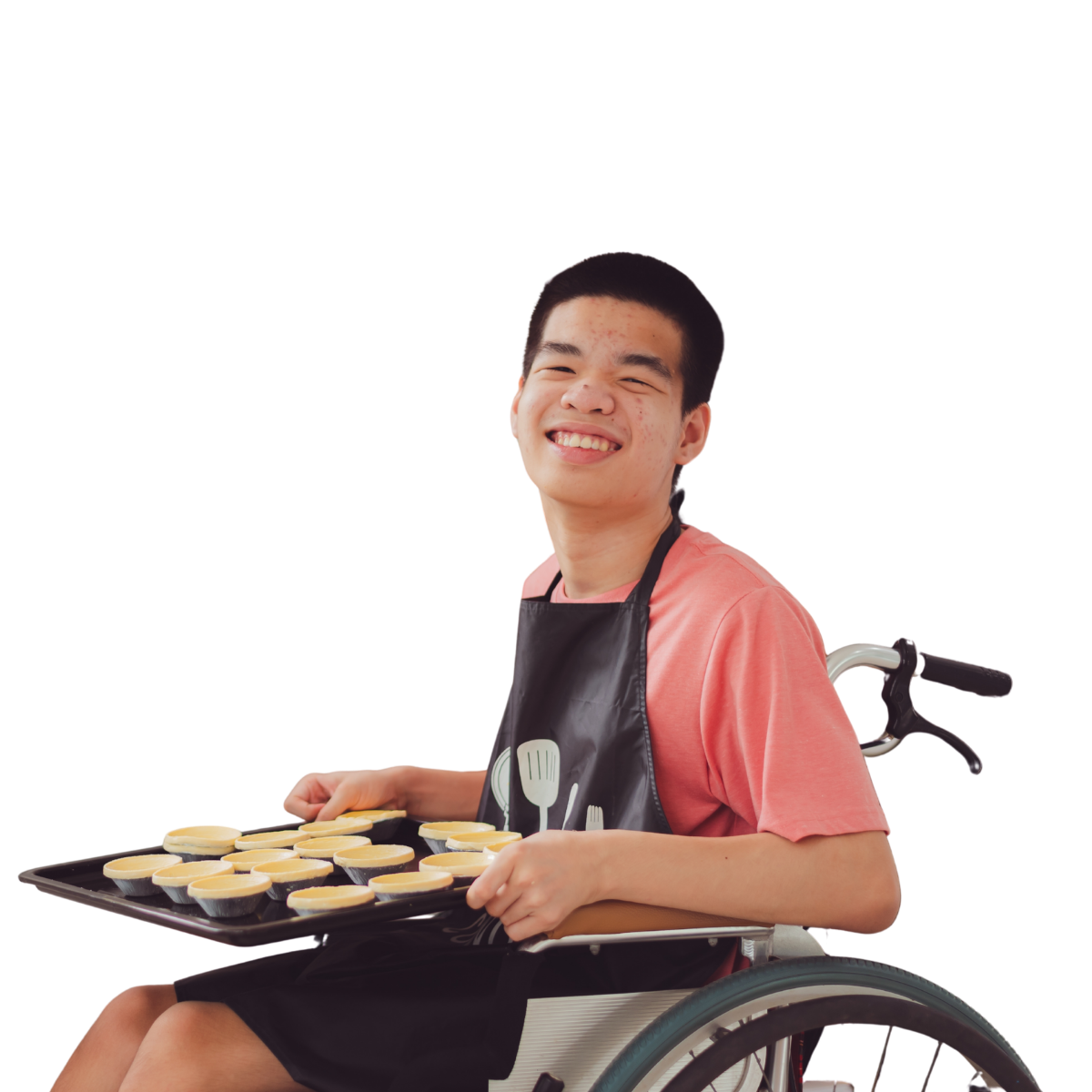 A young man in a wheelchair is smiling whilst holding a baking tray of pastries to go in the oven